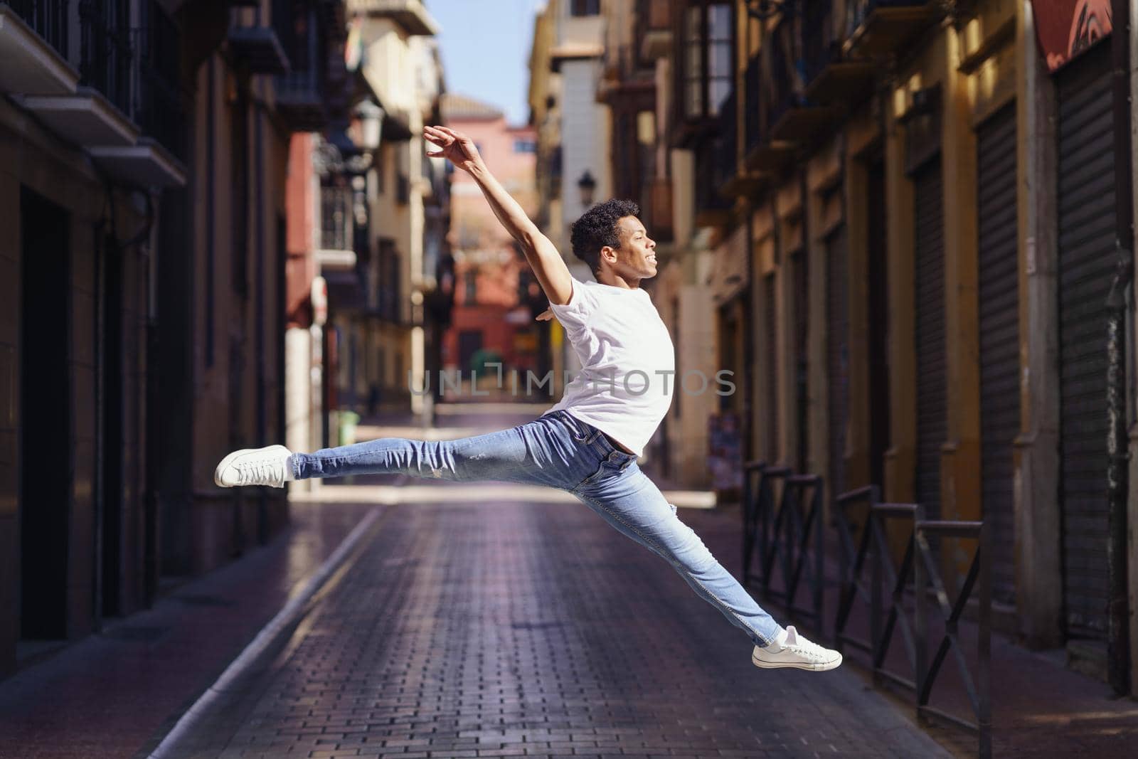 Young black man doing an acrobatic jump in the middle of the street. by javiindy