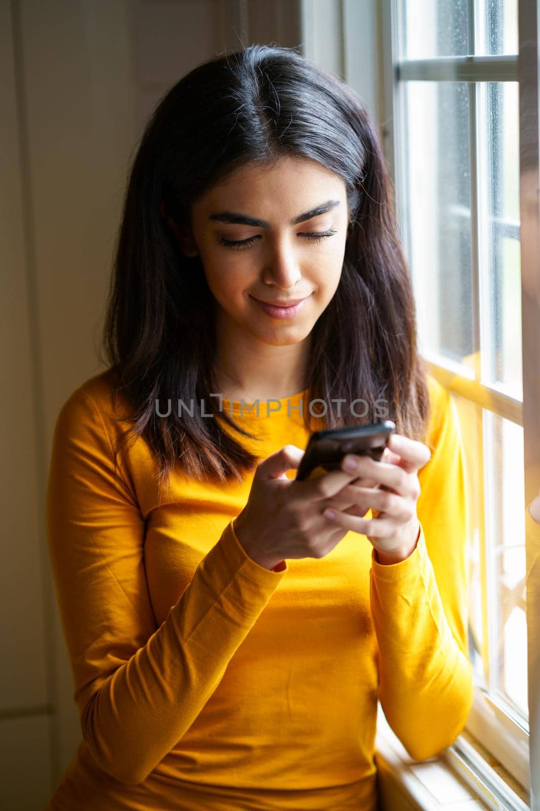 Persian woman at home using her smart phone near the window