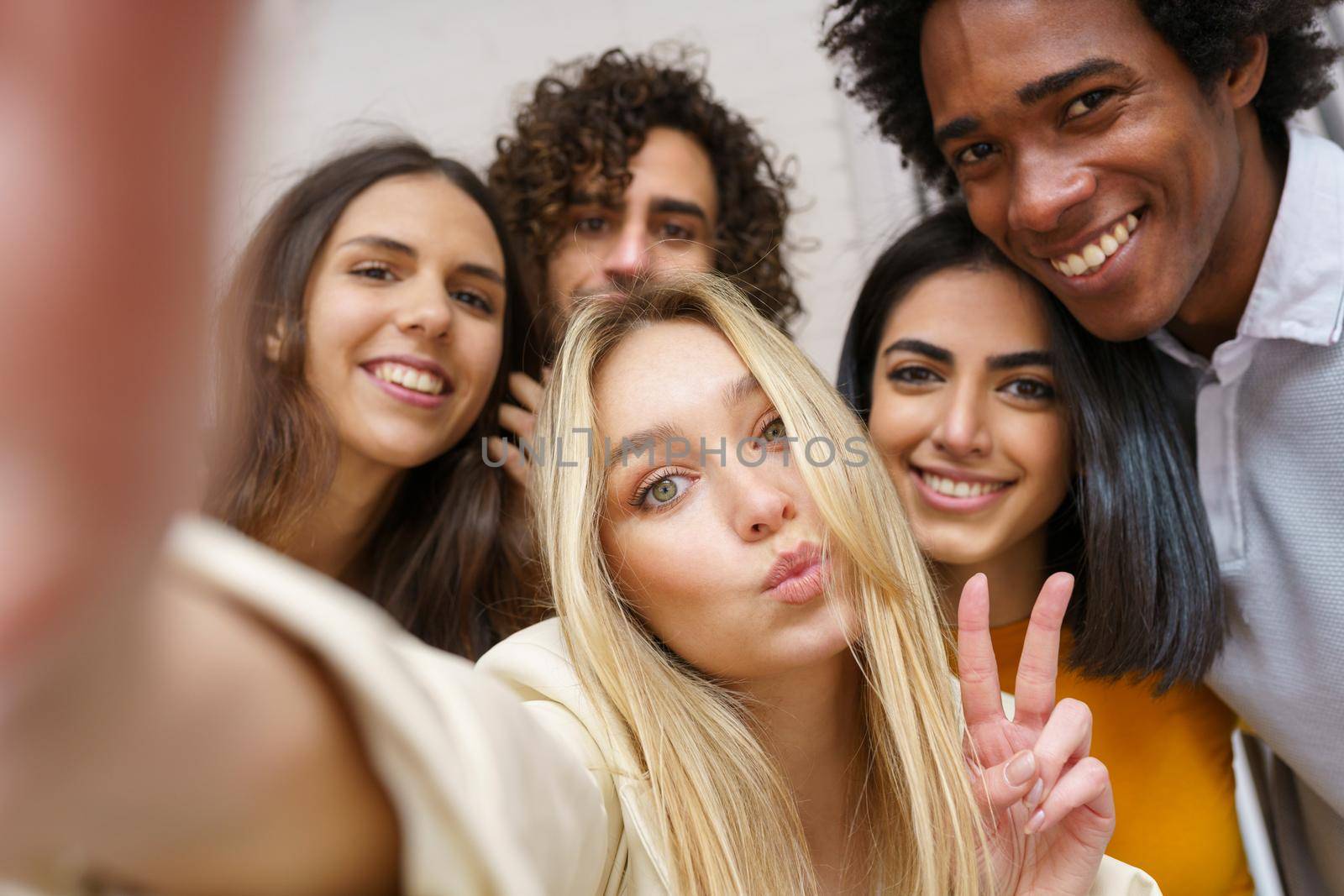 Multi-ethnic group of friends taking a selfie together while having fun outdoors. by javiindy