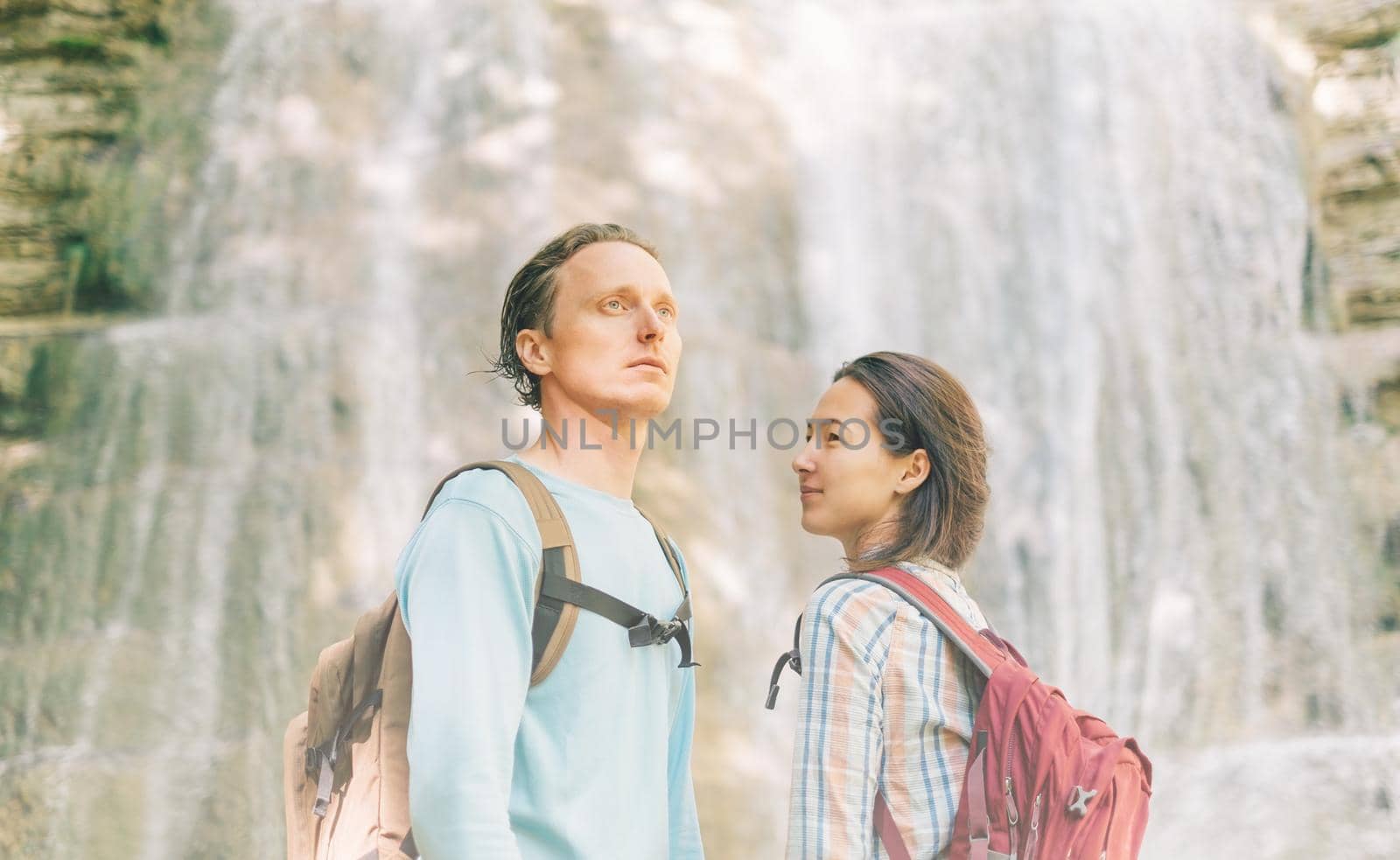 Traveler backpacker young couple standing in front of waterfall in summer outdoor.