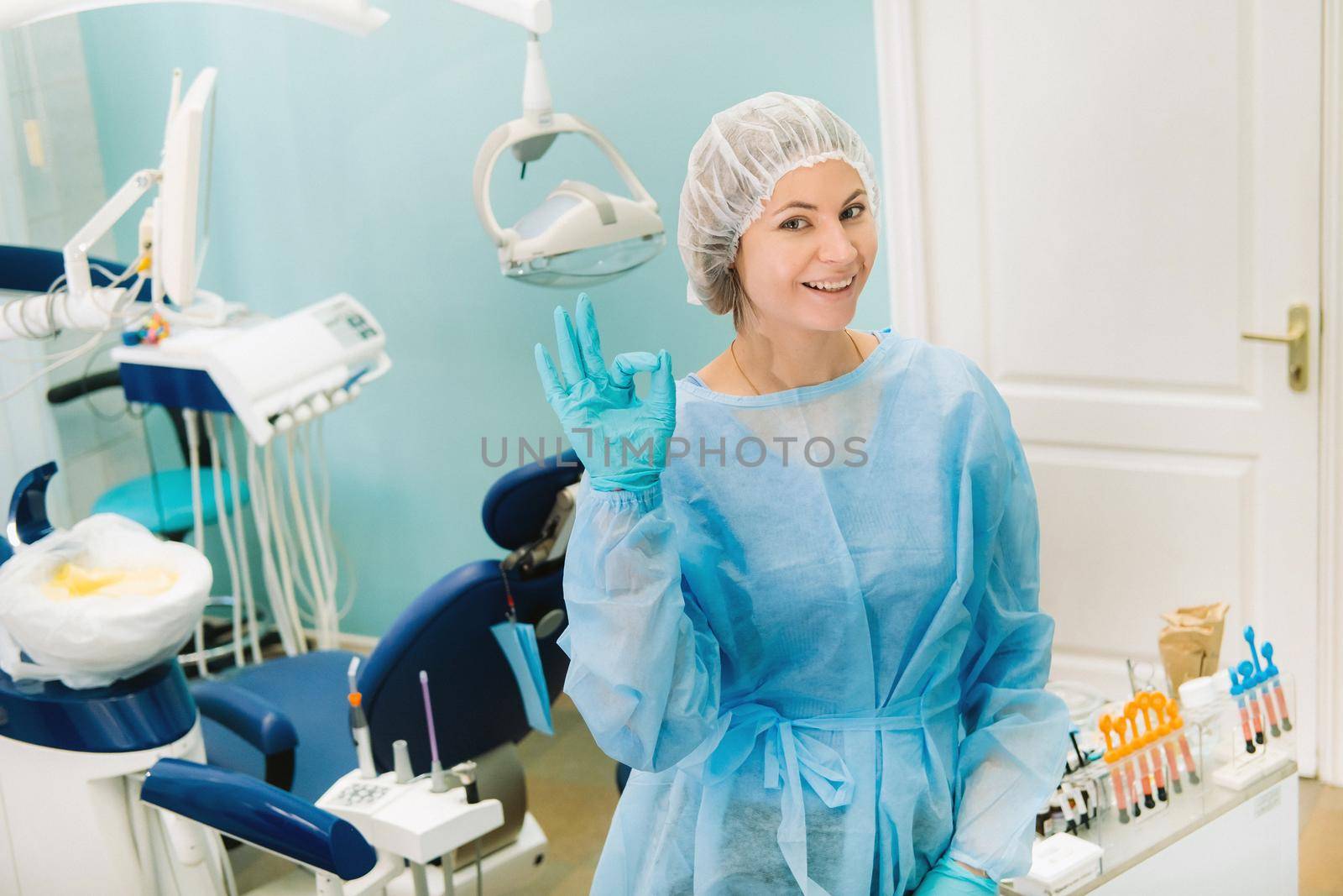 the dentist stands in his office and shows the OK sign.