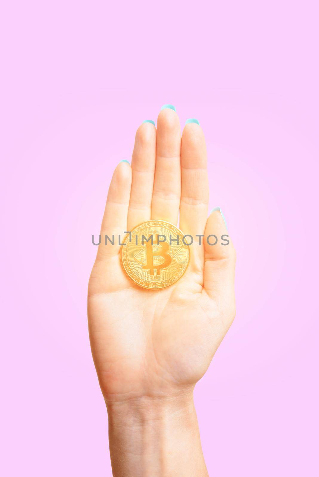 One glowing gold bitcoin on female palm hand on a pink background.