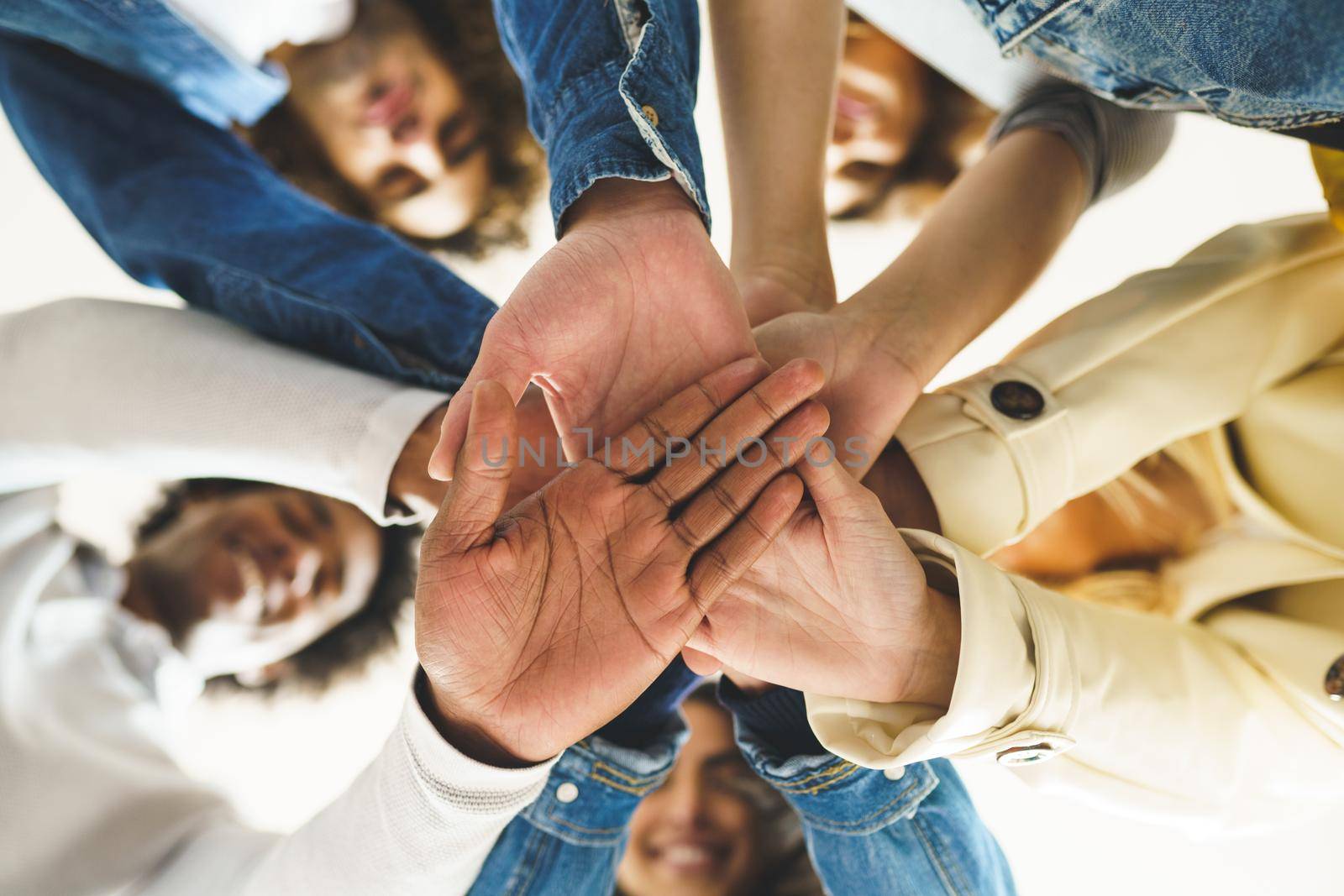 Hands of a multi-ethnic group of friends joined together as a sign of support and teamwork. Young people having fun together.
