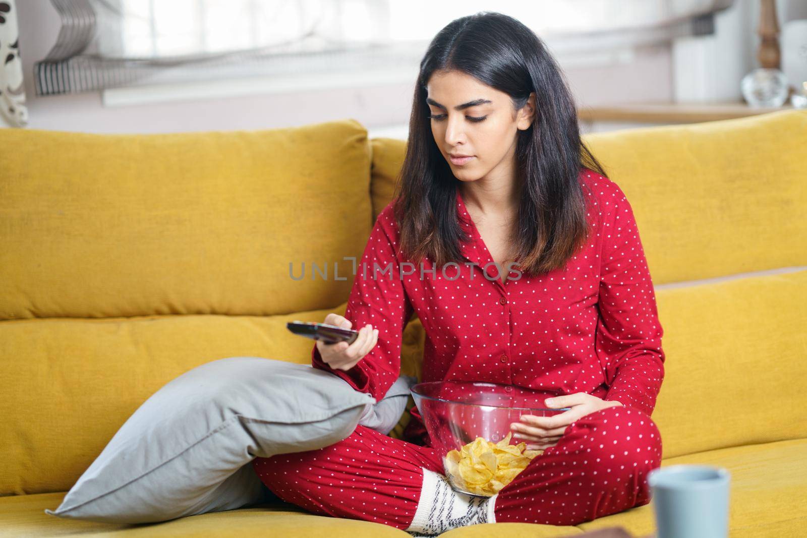 Persian woman at home watching TV and using remote control by javiindy