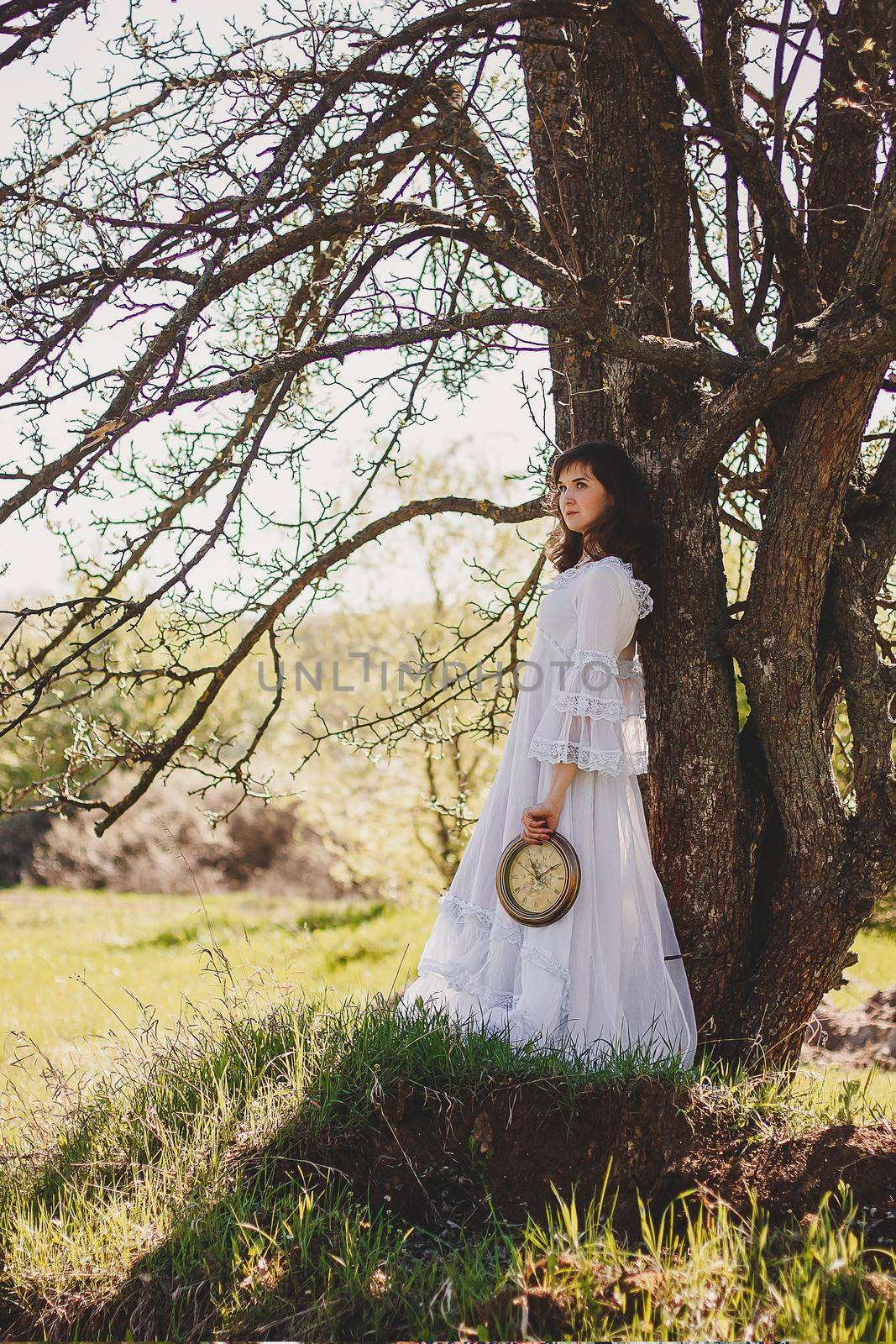 Portrait of carefree young woman in white vintage wedding style dress in spring cherry blossom garden valley.