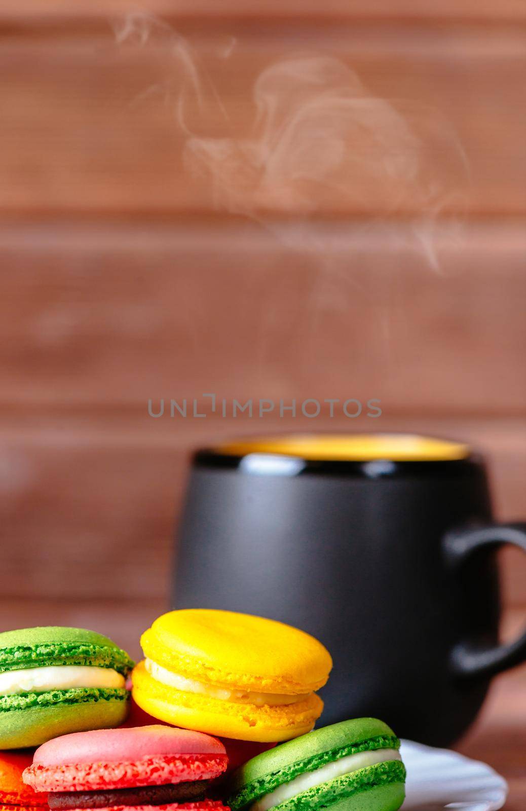 Colorful macarons cookies and cup of hot drink on a wooden background.