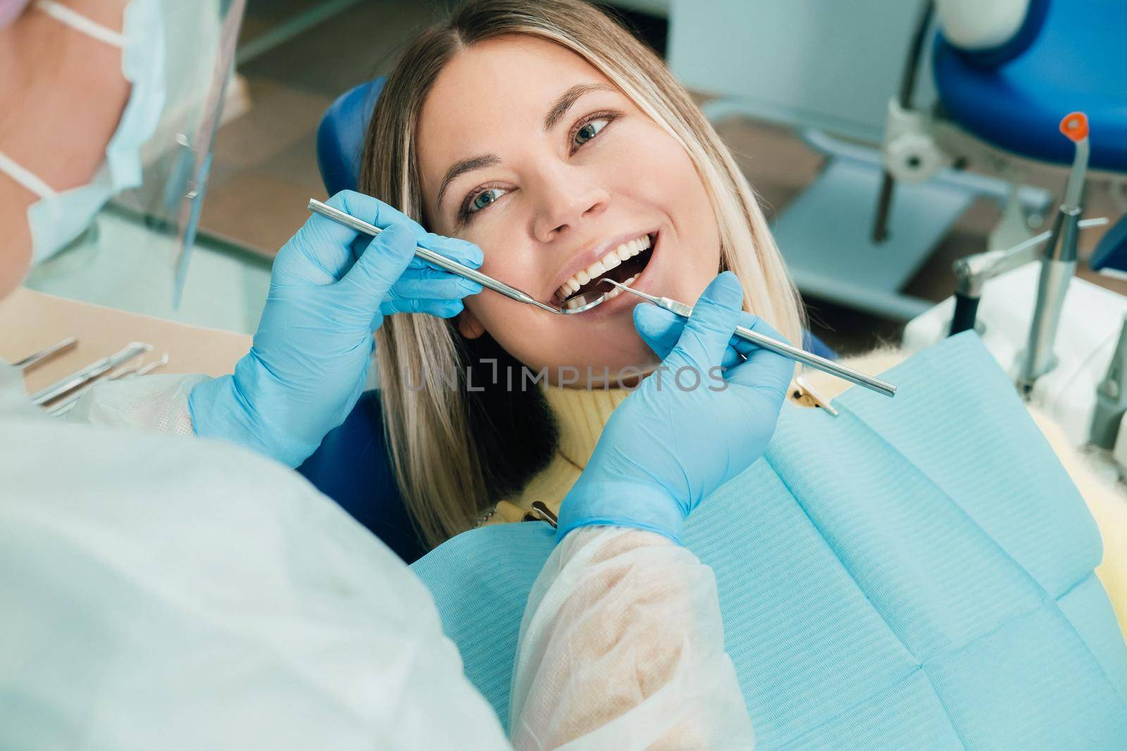 a dentist in a protective mask sits next to him and treats a patient in the dental office.