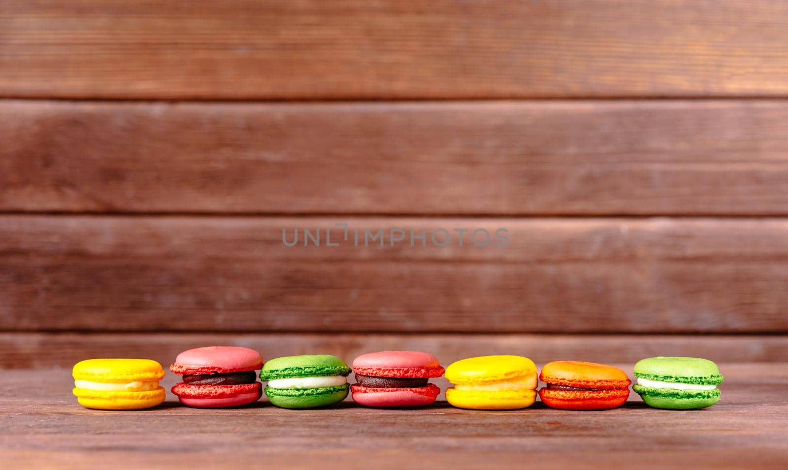 Colorful sweet macarons dessert in a row on wooden table. Copy-space in upper part of image.