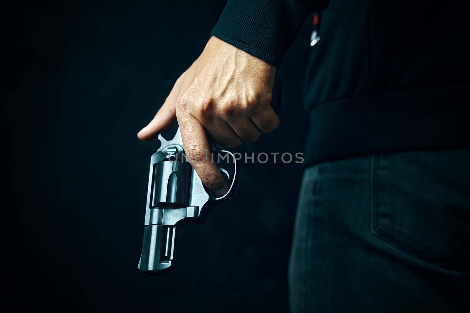 Black revolver with drum in man's hand. Guy with gun down. Firearms for attack or defense. Armed person on dark background.