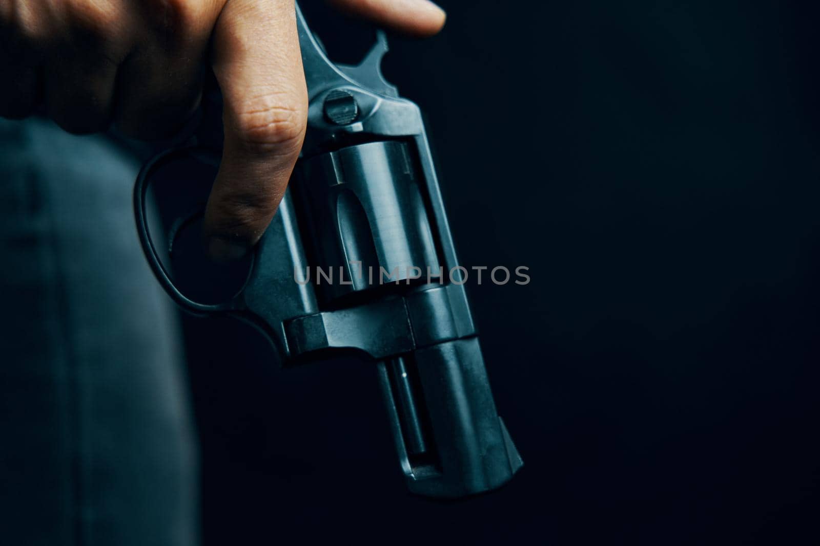 Black revolver with drum in man's hand. Armed person on dark background. Guy with gun down. Firearms for attack or defense.