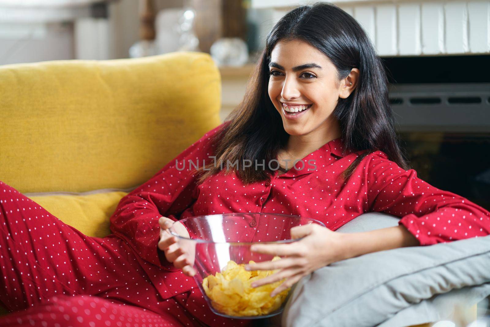 Persian woman at home watching TV. Girl eat chips potatoes