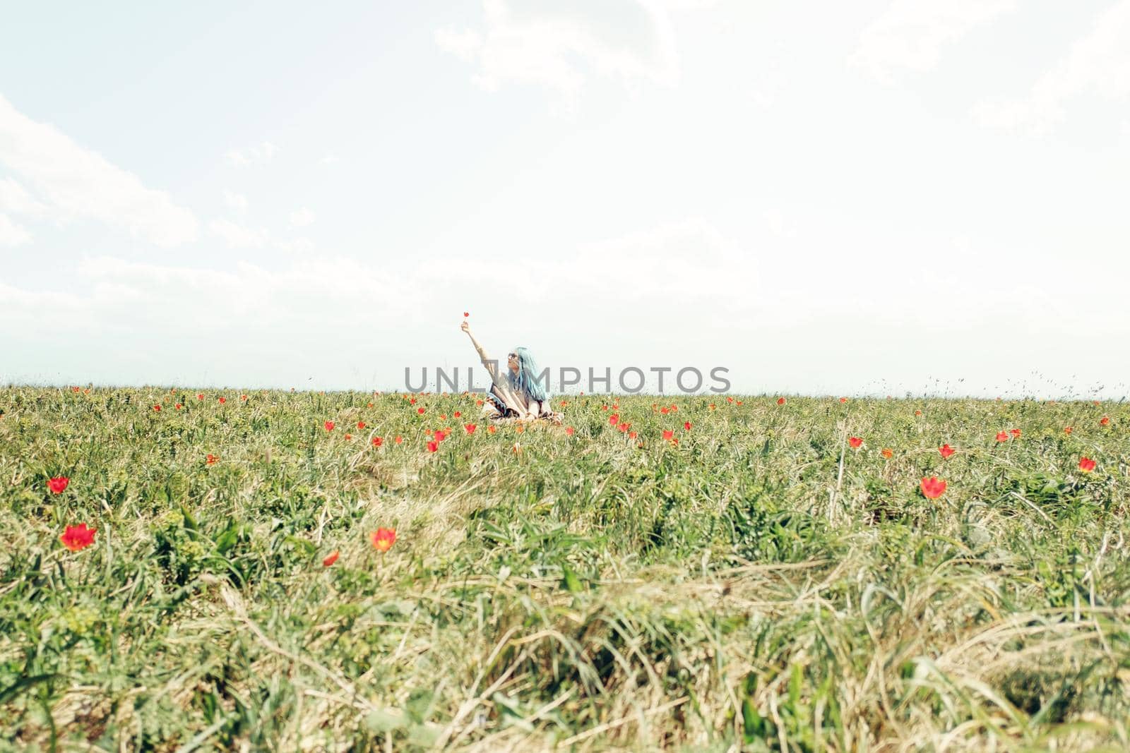 Happy young woman resting on meadow with red tulips in summer.