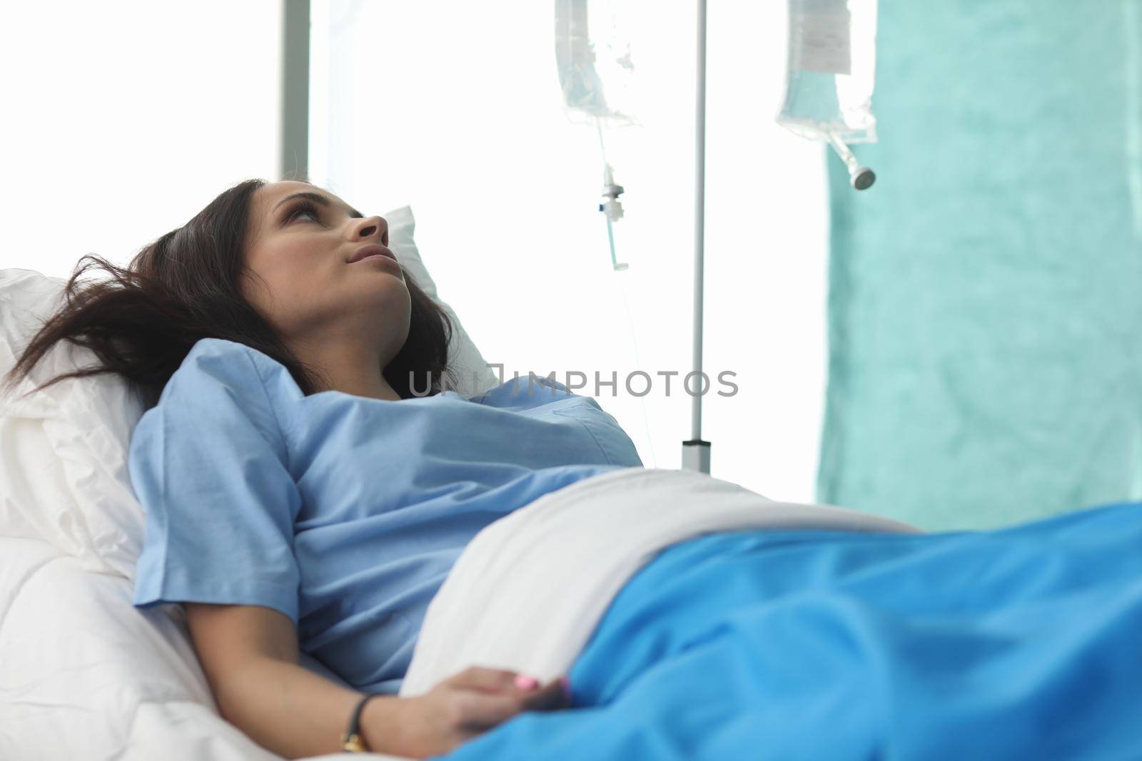 Closeup of young woman laying in hospital bed and waiting for analysis. Clinic patient. Treatment with drop bottle. Medicine and health diagnostic concept