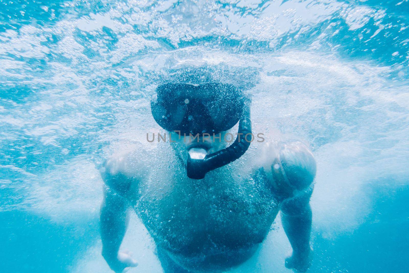 Sporty young man freediver in mask and snorkel swimming underwater surface.
