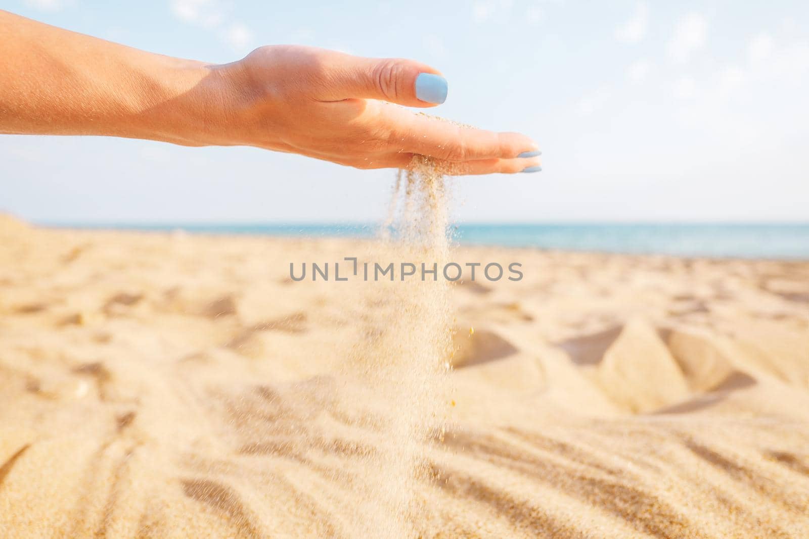 Sand flowing through female hand on beach near the sea.
