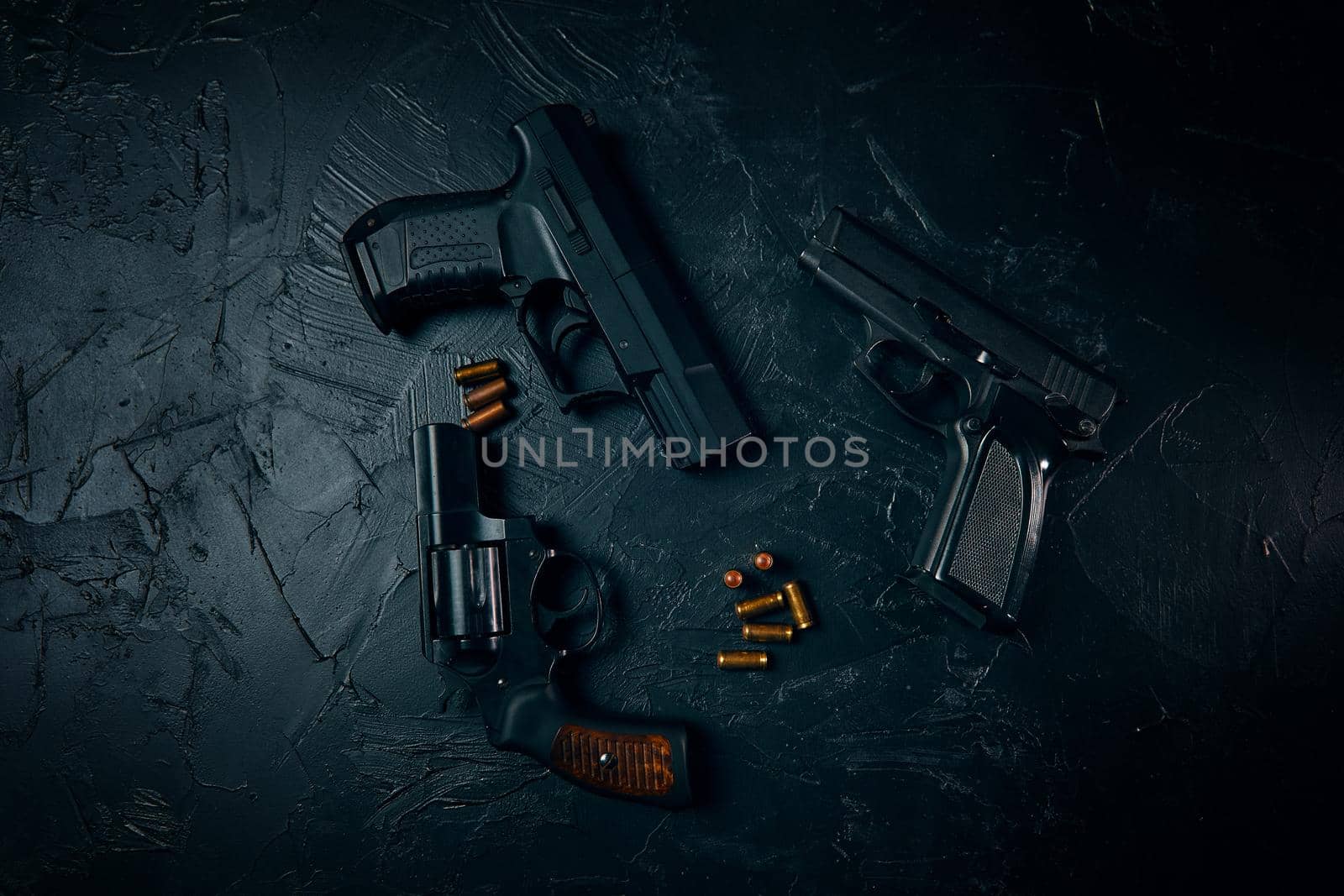 Top view of pistols and gold bullets on black table. Criminal or police arsenal. Dangerous firearms. Vintage revolver with a drum. 9mm hand gun.