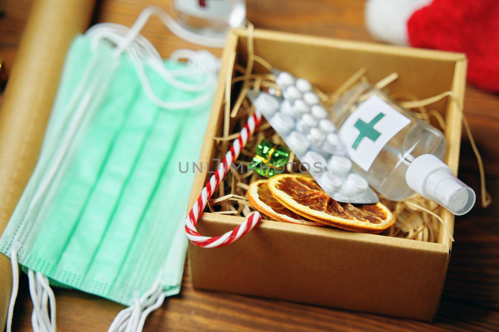 Gift box with antiseptics, pills, lollipops and dried oranges. Christmas surprise and medical masks on a wooden table. New Year's Eve during pandemic. Holidays in quarantine.