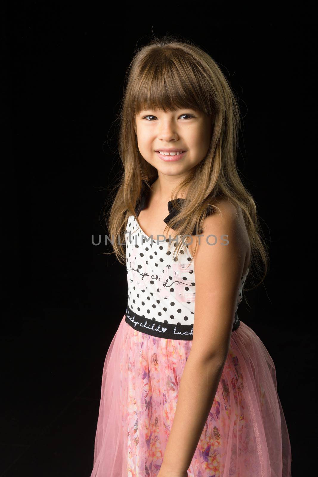 Portrait of a cheerful girl in stylish summer clothes. Front view of a beautiful girl in a sundress and a headband posing on a black background and smiling at the camera