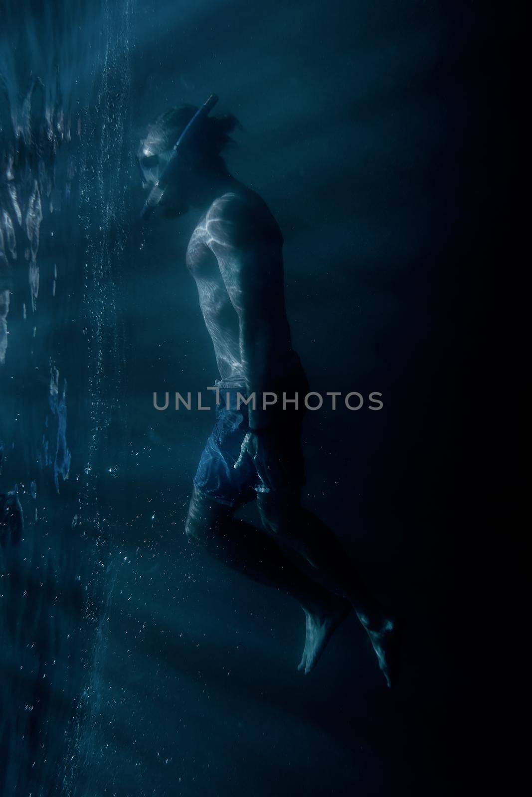 Young man freediver in mask with snorkel swimming underwater near the surface. Concept of magical portal into another world.