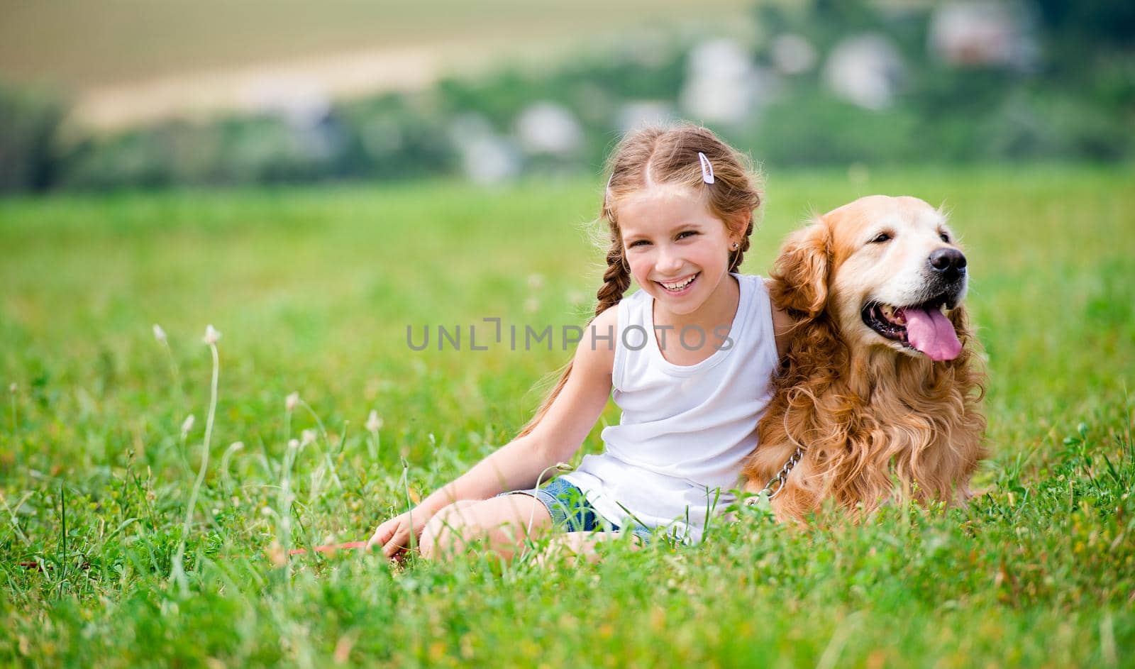 Smiling Little girl sitting on the grass with golden labrador