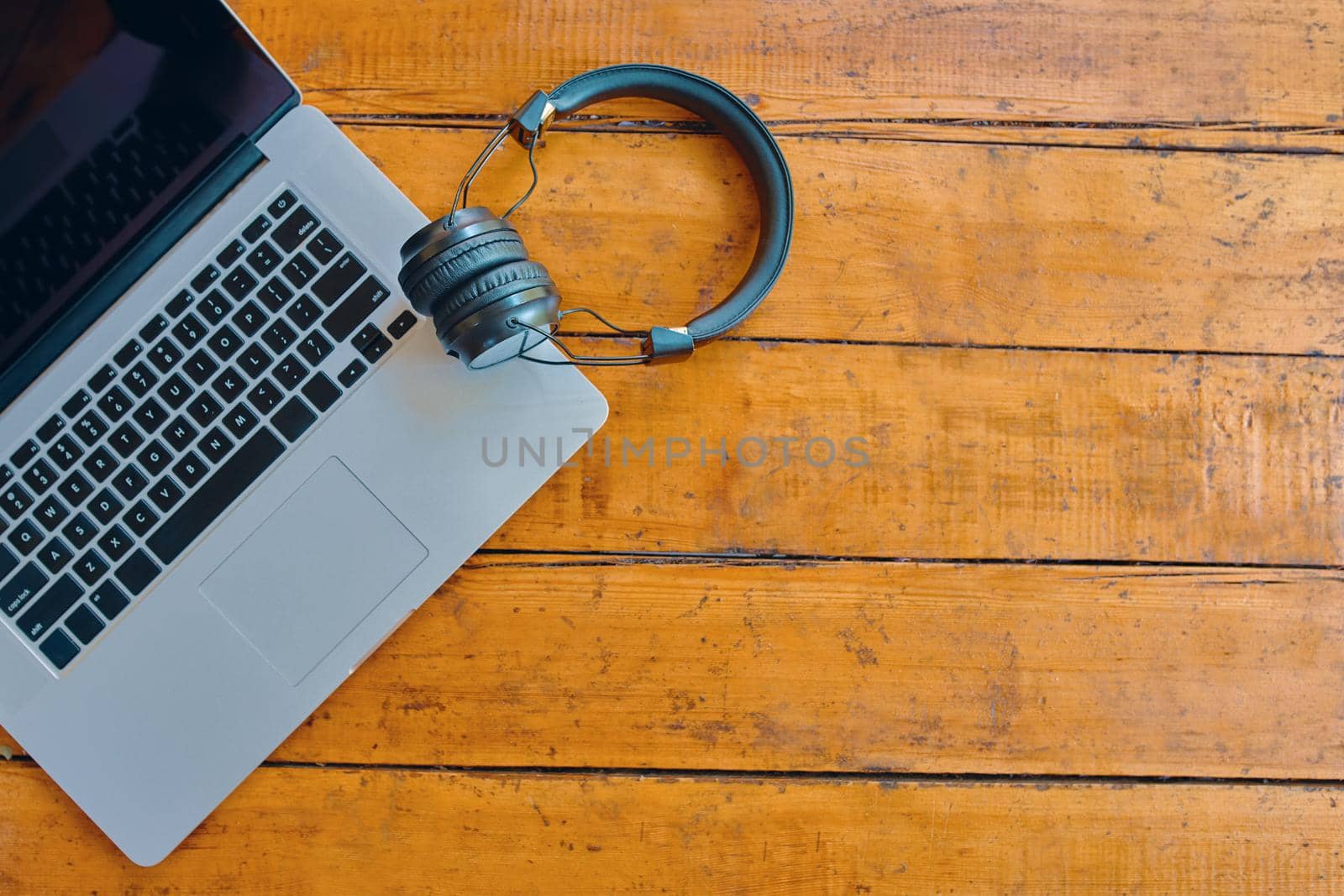 Flat lay of laptop and wireless headphones on wooden table. Notebook with black screen. Copy space for text. Workspace of freelance. English keyboard.