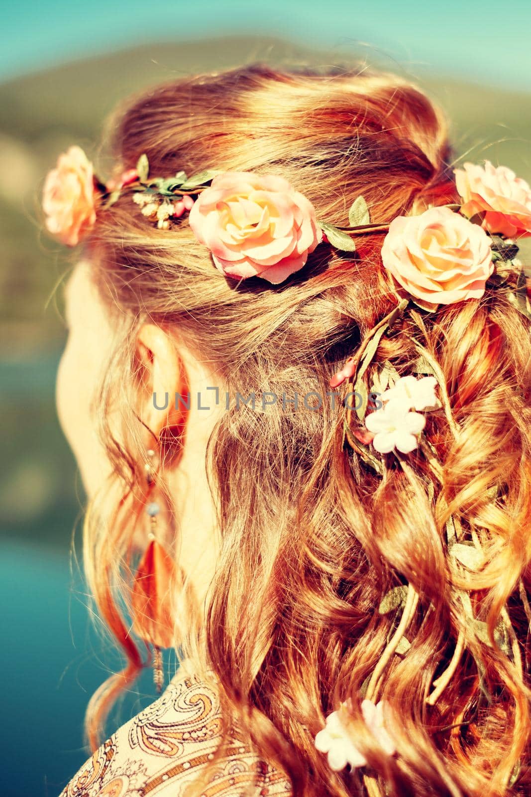 Young redhead woman with curly hairstyle and flowers outdoor.