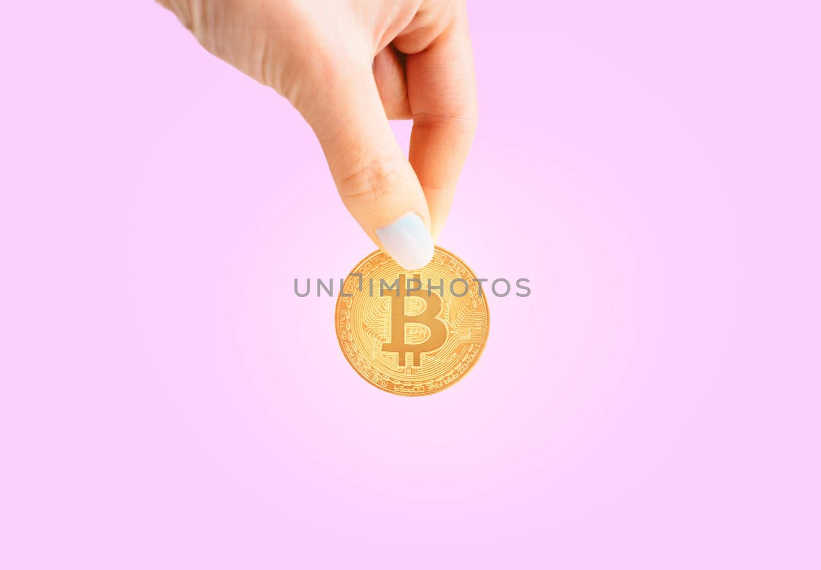 Woman’s hand with glowing gold bitcoin on a pink background, copy-space for text.