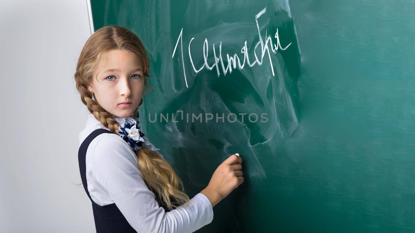 Schoolgirl writing on chalkboard in classroom. Primary school student in uniform standing in front of blackboard and writing using chalk. Back to school, education concept