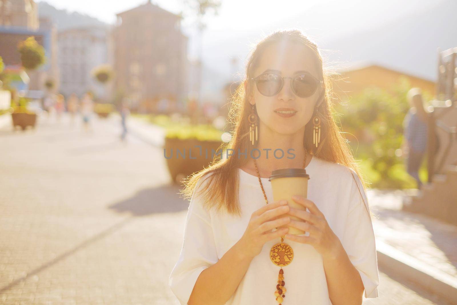 Stylish smiling beautiful young woman walking on the street with cup of coffee.