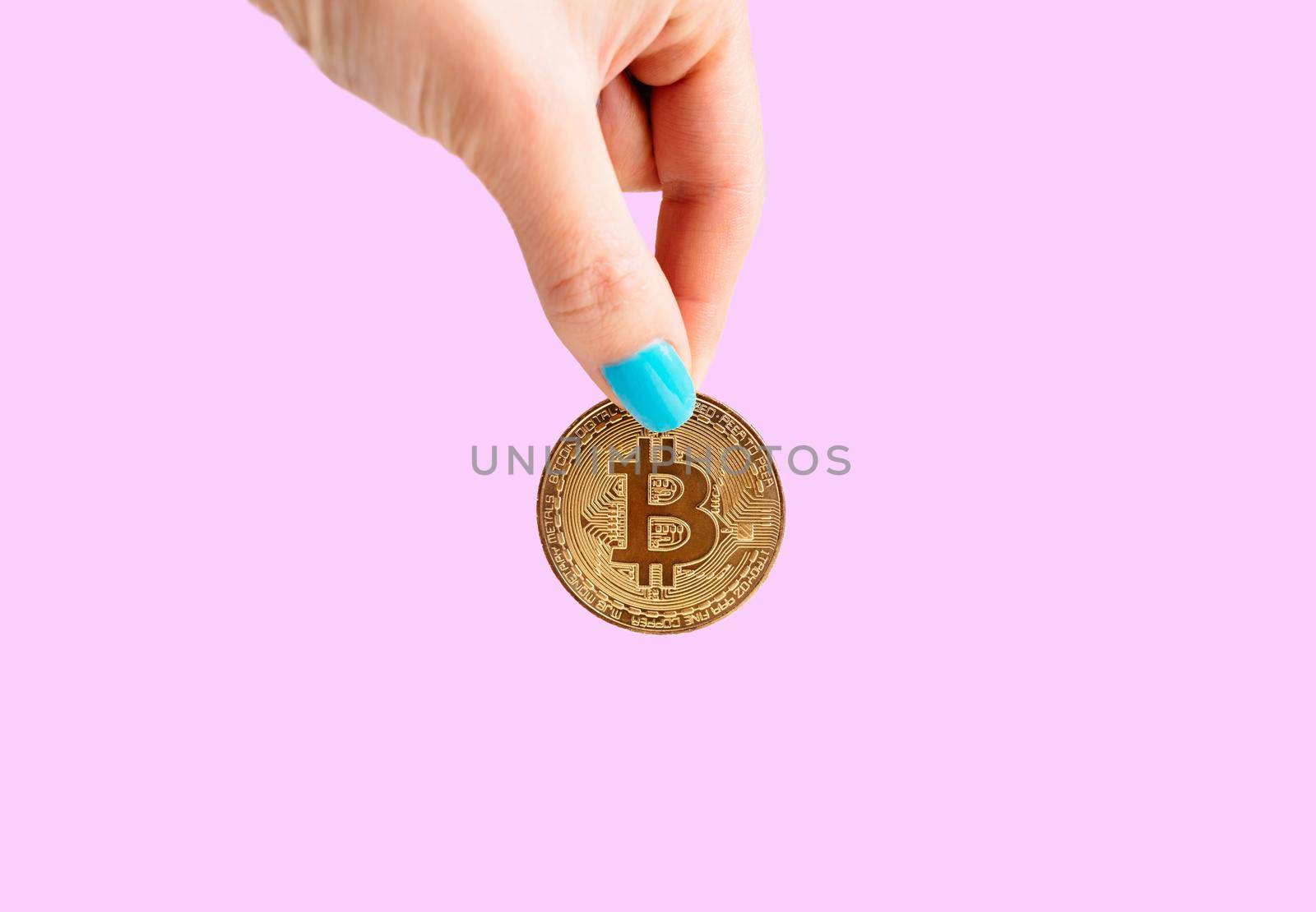Woman’s hand with gold coin bitcoin on a pink background, symbol of virtual money.
