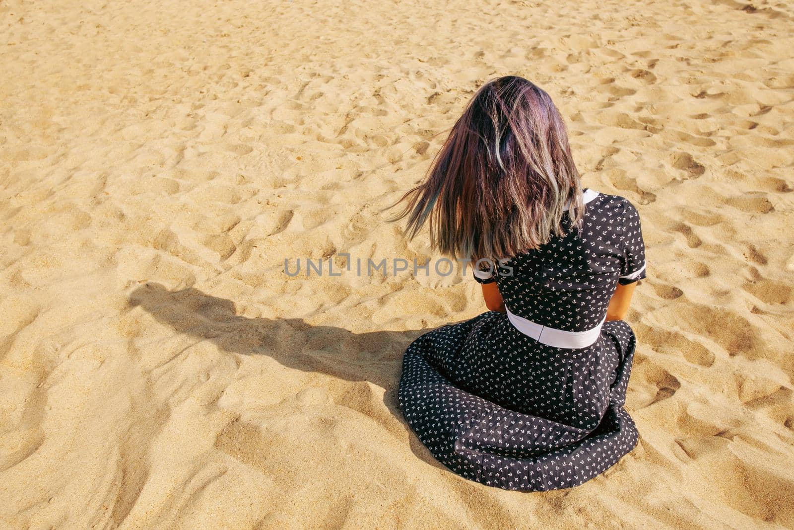 Unrecognizable young woman resting on sand, rear view.