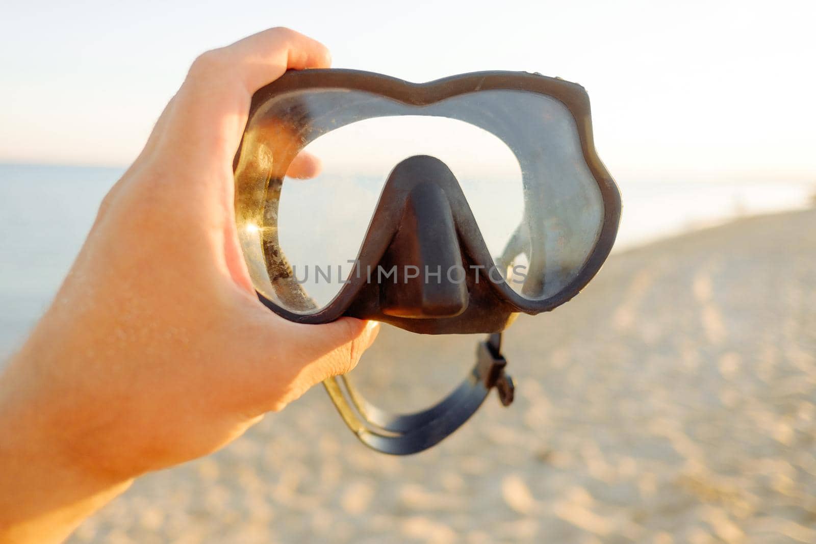 Male hand holding mask for swimming on background of sea outdoor, point of view.