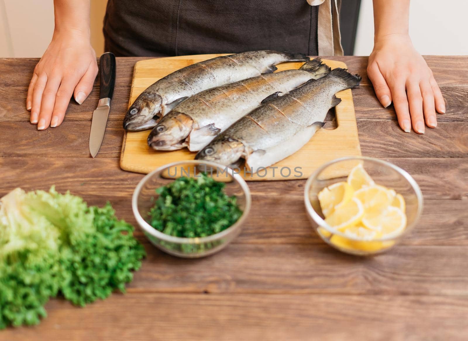 Woman will cook fish trout, hands on kitchen wooden table near the ingredients of dish.