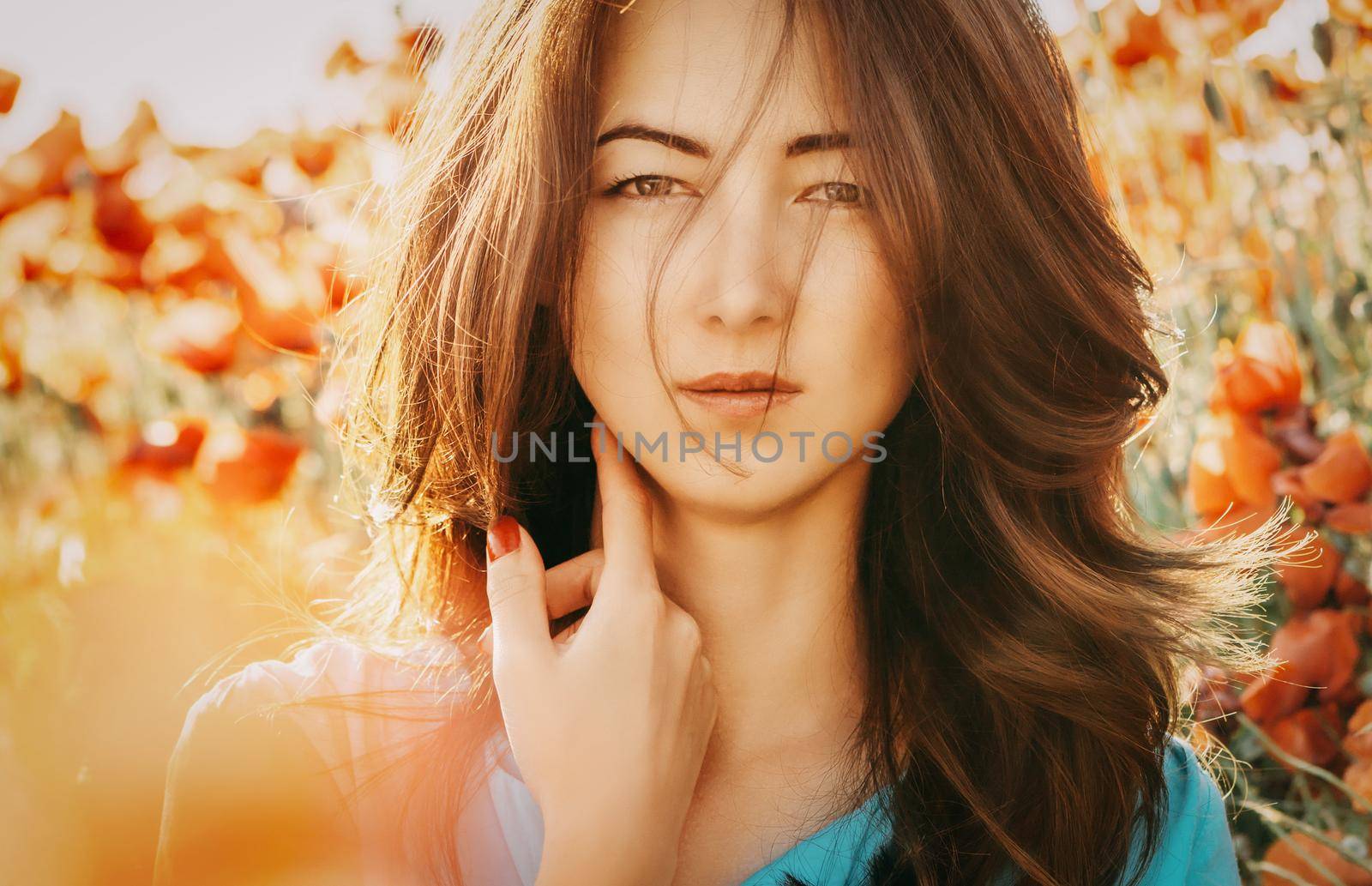 Portrait of beautiful brunette young woman on background of poppies flowers, looking at camera.