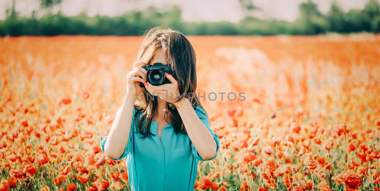 Young woman taking photographs with camera in poppies flower meadow in summer outdoor.