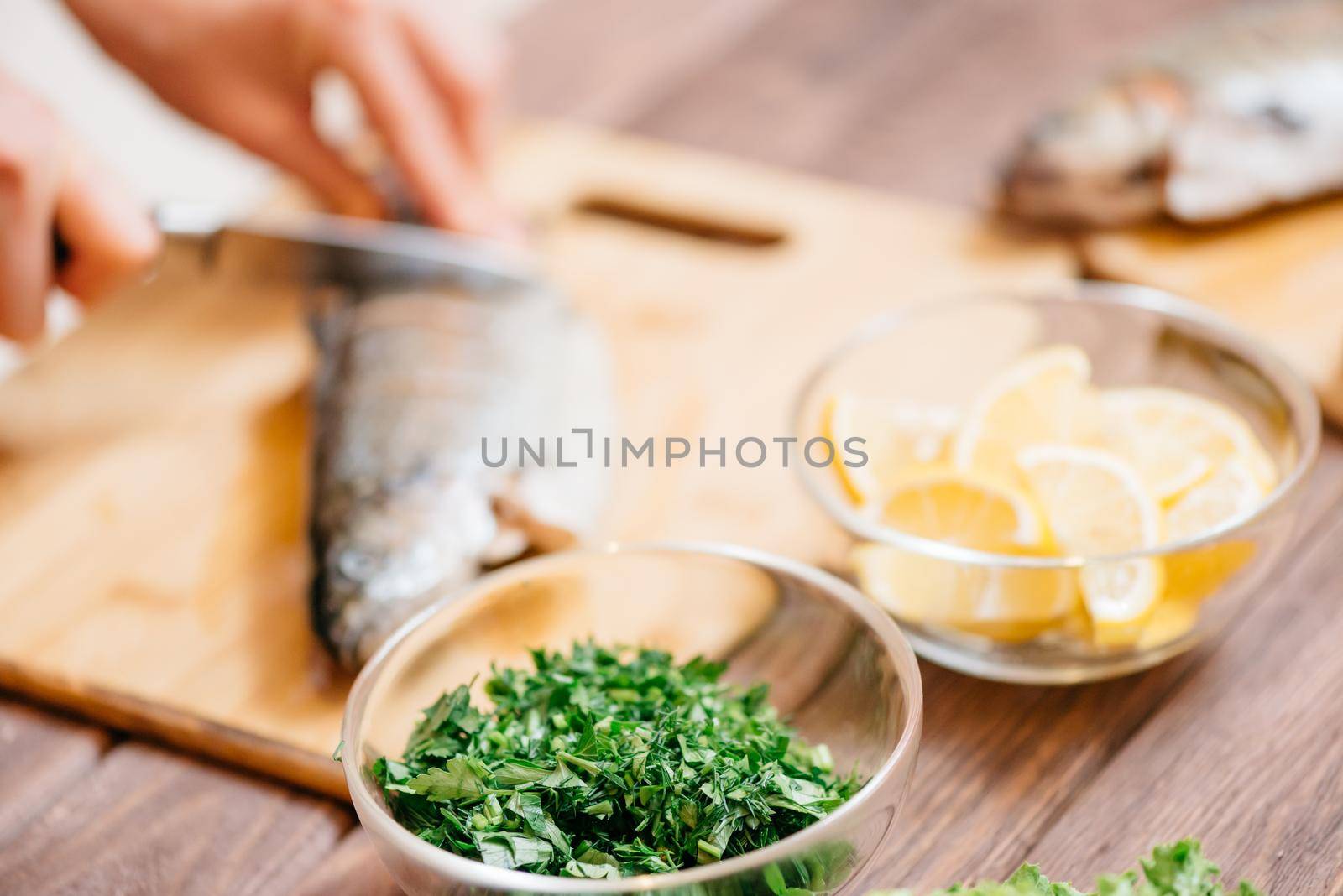 Woman cutting raw fish for dish in the kitchen near food ingredients. Focus on foreground.