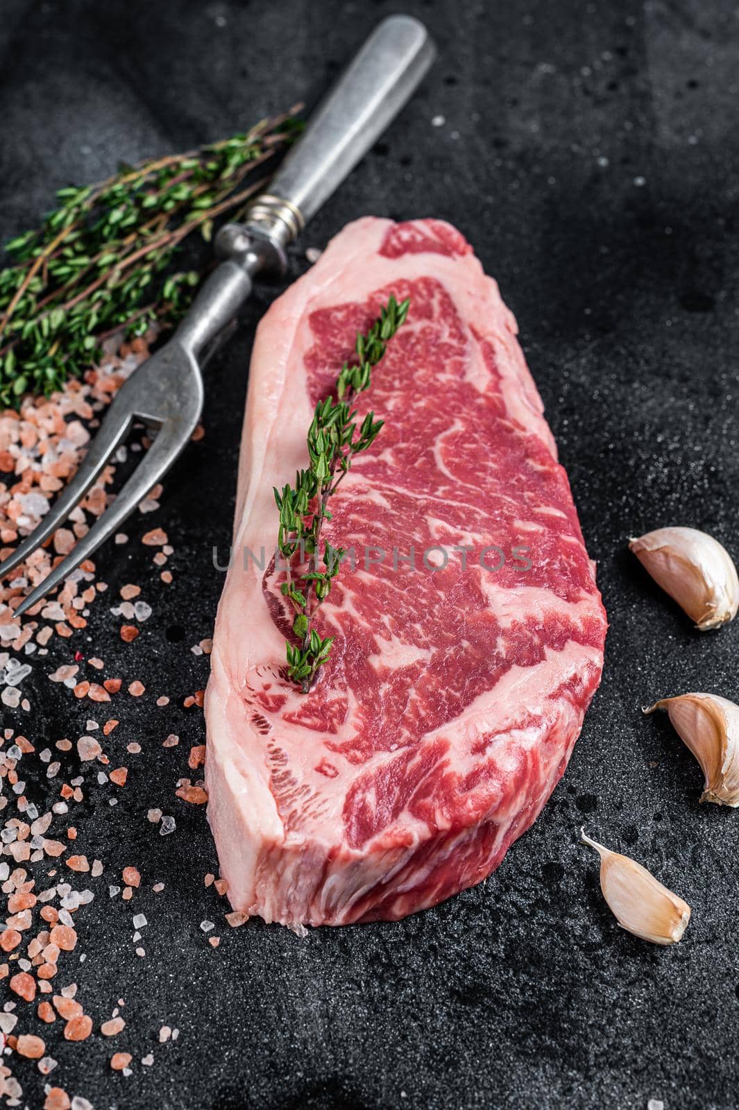 Raw striploin steak on a butcher table with salt and thyme. Black background. Top view.