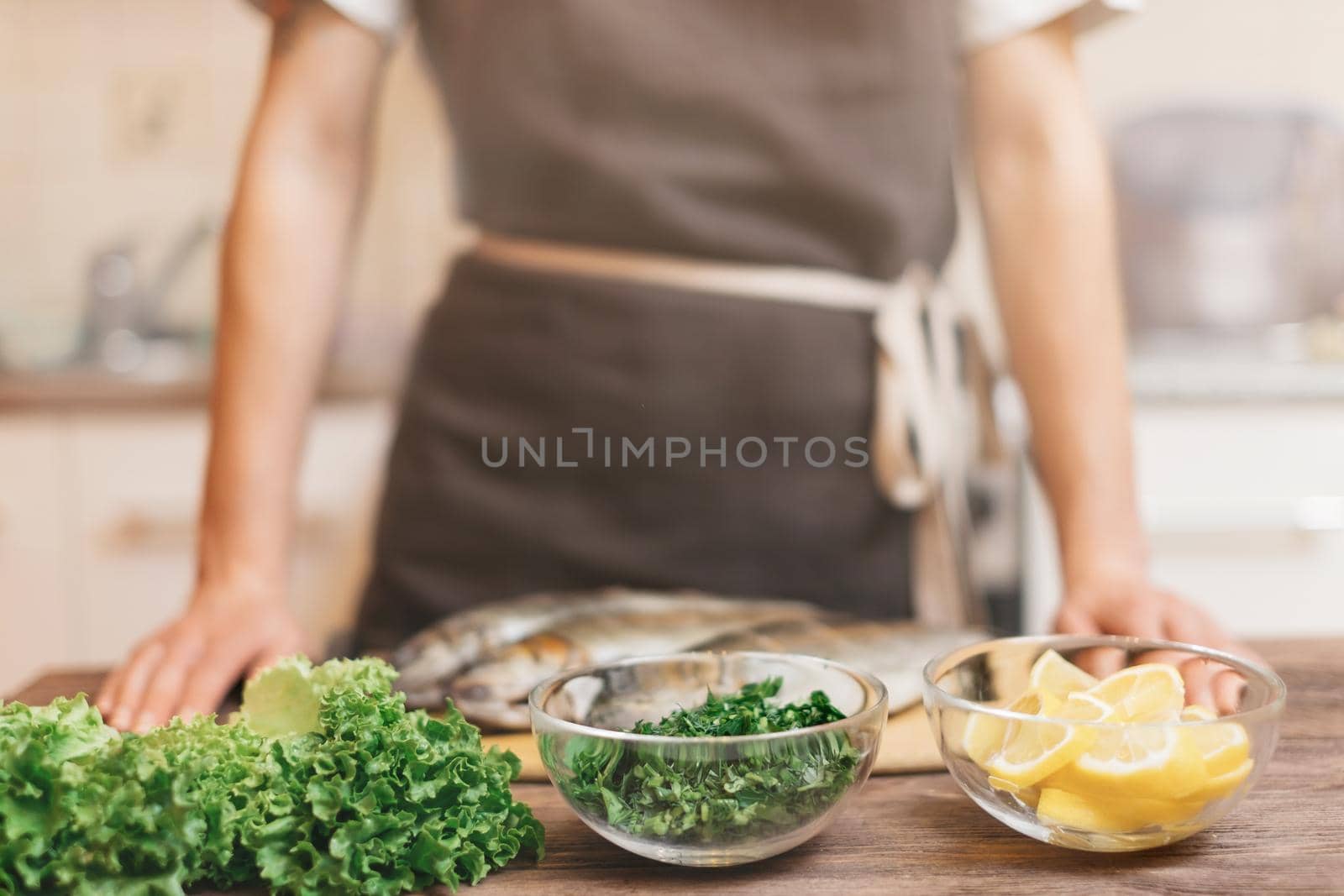 Woman cooking in the kitchen, ingredients for fish dish on wooden table. Focus on foreground.