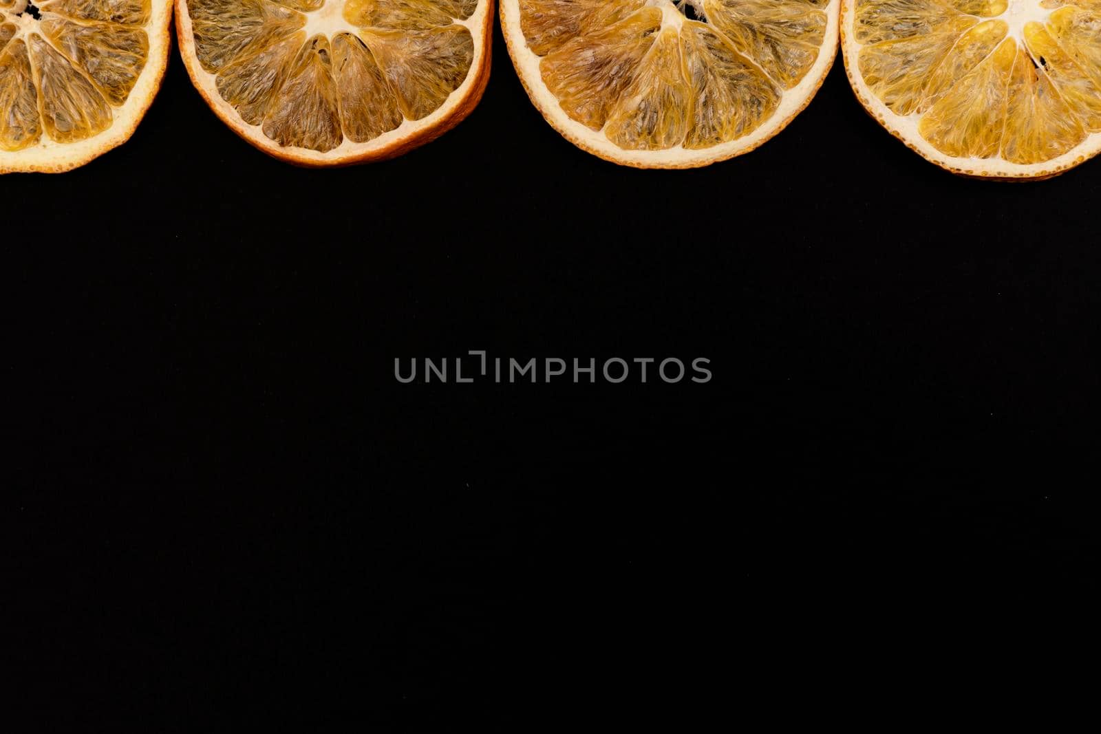 Sliced dried oranges at the top of black background, copy space, a lot of place for text, view from the top.