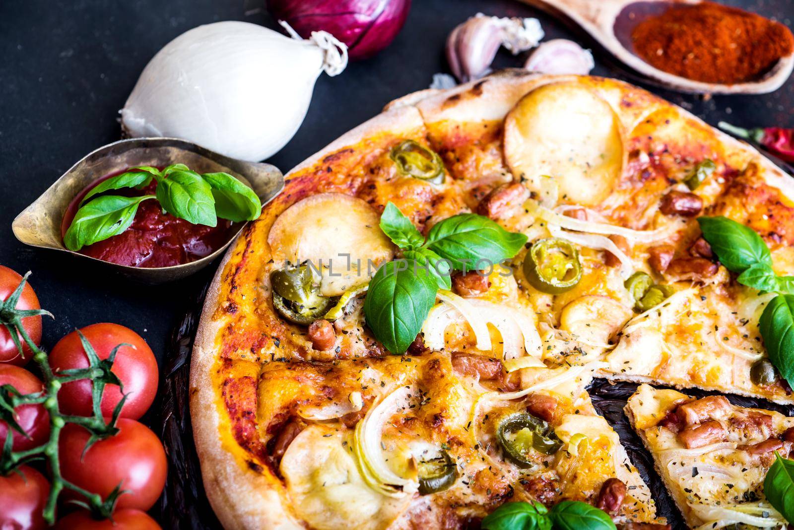 tasty pizza on a black background with spices and vegetables