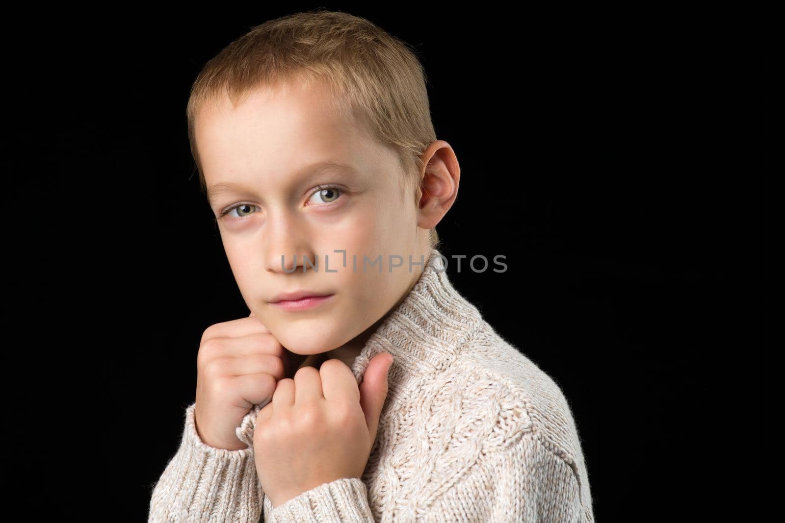 Portrait of cute teenage boy. Handsome stylish boy in hat and knitted jumper covering his face with hands. Preteen child posing in studio against black background