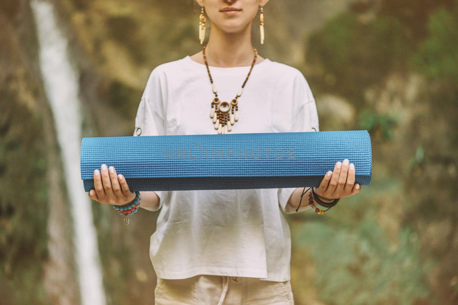 Young woman standing with yoga mat in summer outdoor.