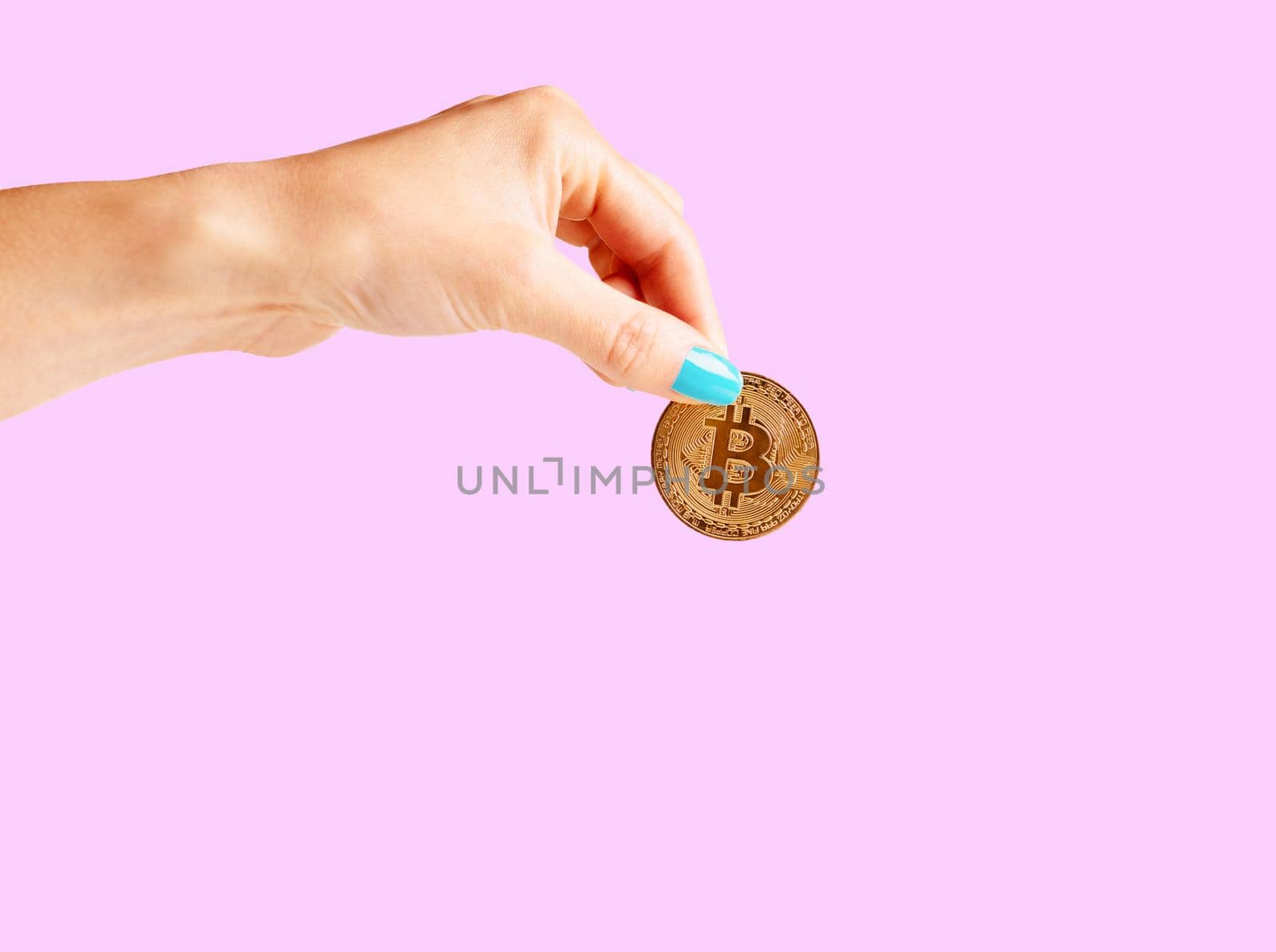 Woman’s hand holding gold coin bitcoin on a pink background, symbol of virtual money.