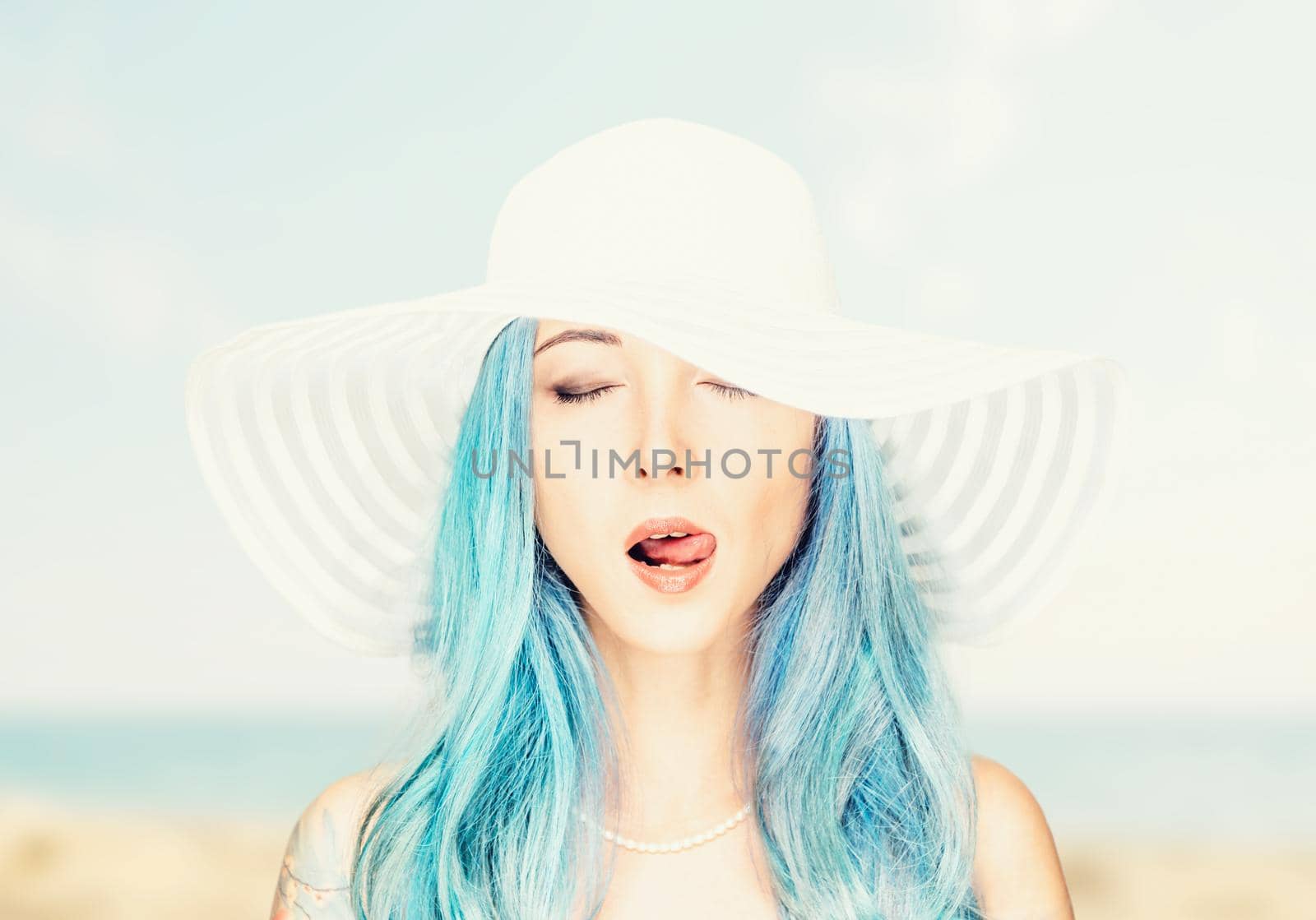 Portrait of beautiful sensual young woman with blue hair in a hat on background of sea.
