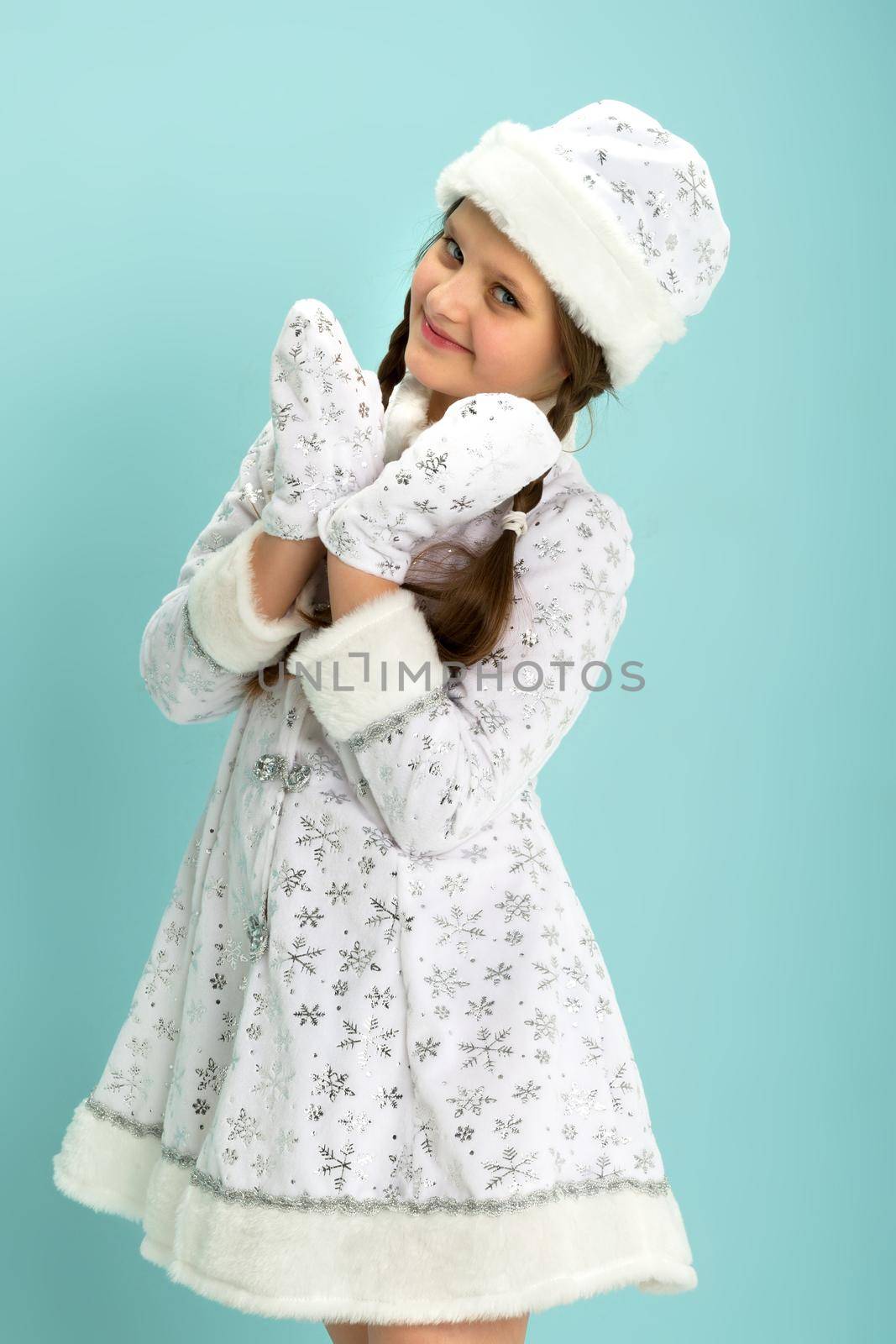 A beautiful girl dressed as a Snow Maiden. Adorable little girl in a white hat and a fur coat embroidered with silver threads, posing in the studio. On Blue Background.New Year and Christmas, Winter Holidays Celebration Concept