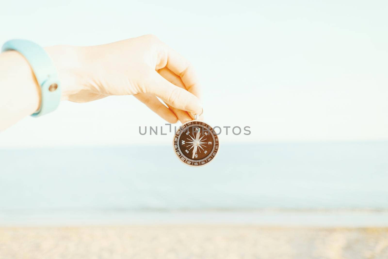 Female hand holding magnetic compass on background of sea, point of view.