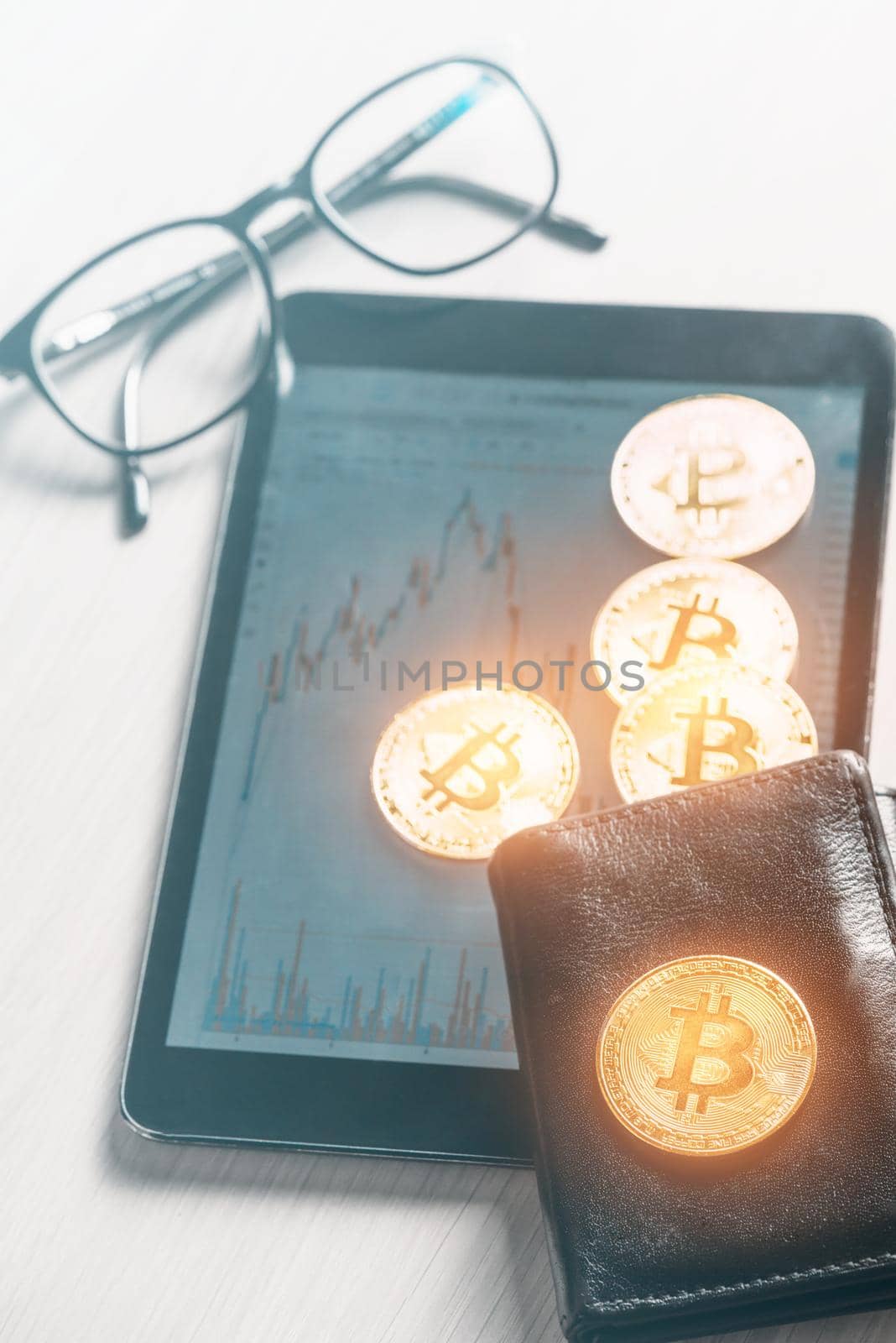 Glowing gold bitcoins on wallet and digital tablet with diagram near glasses, business workspace.