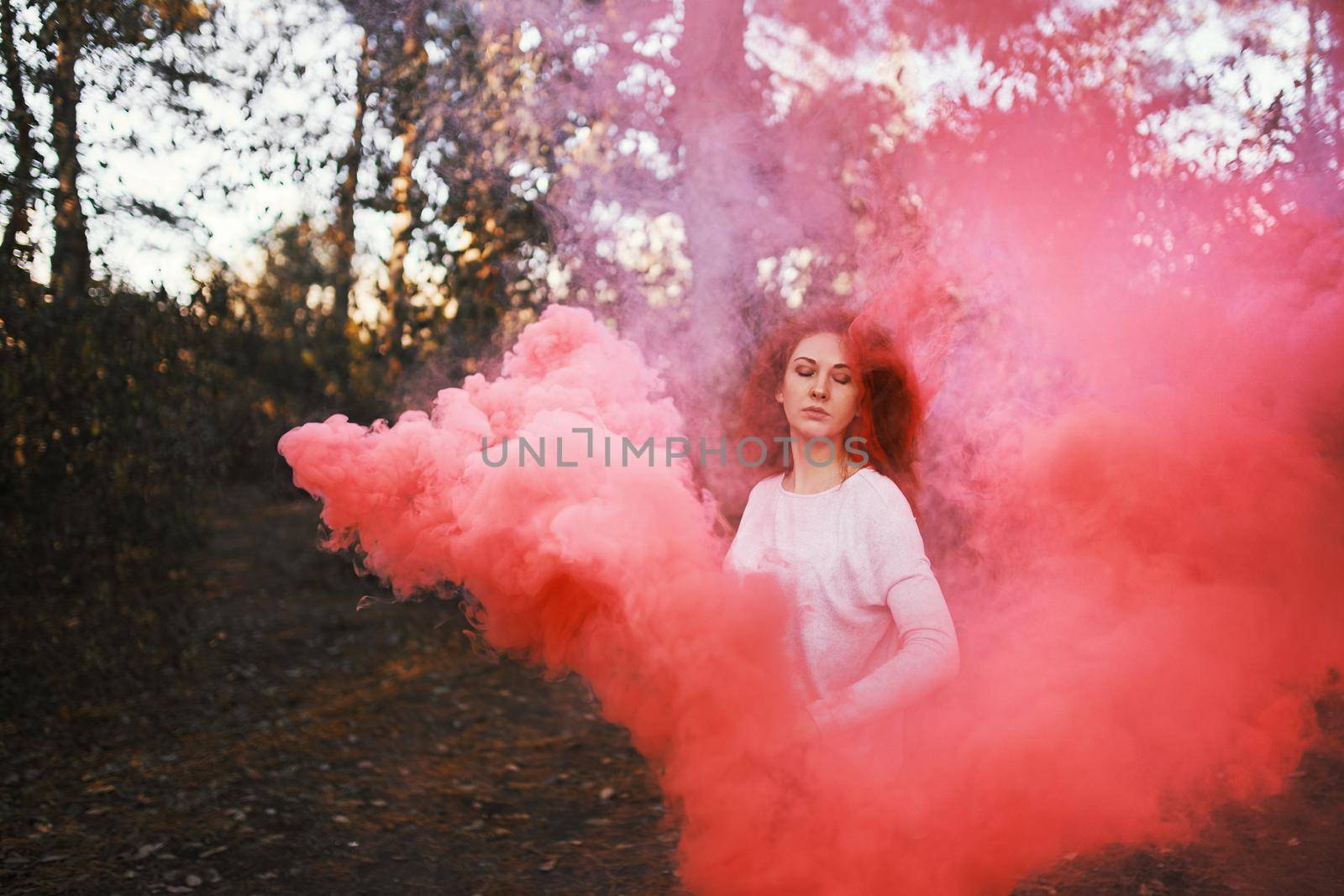 Smoke screen in the woods. Woman with smoke. Beautiful woman with pink smoke behind her in the forest