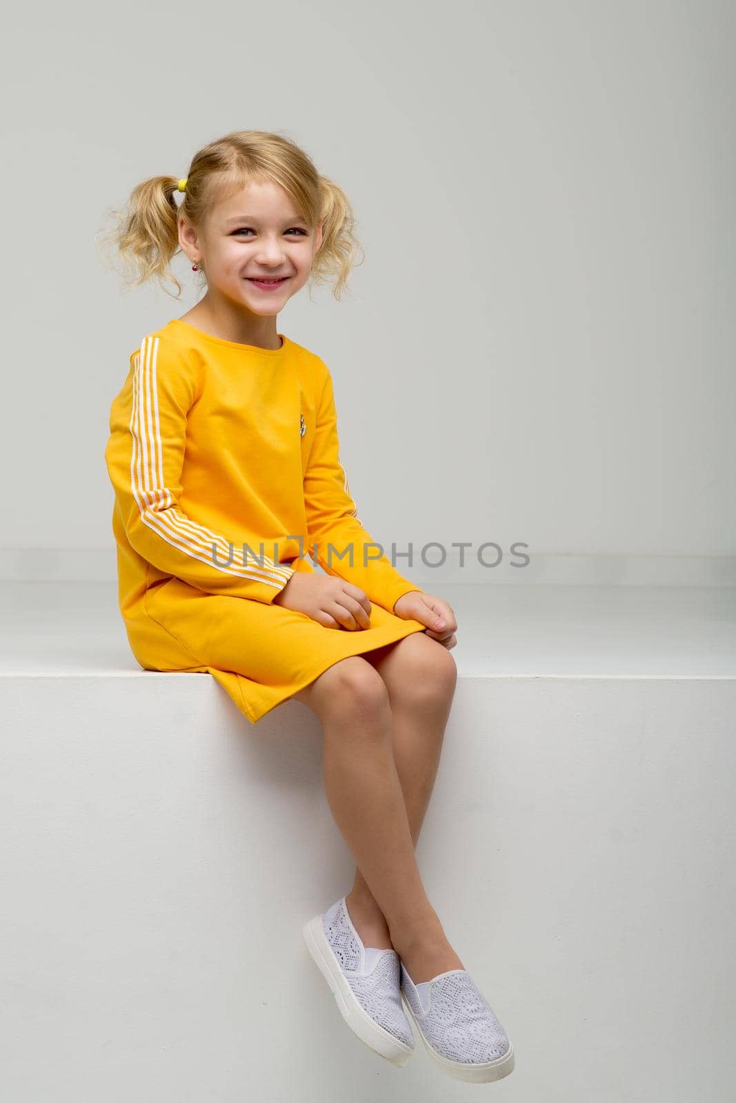 Cute little girl is sitting in the studio on the white floor. by kolesnikov_studio