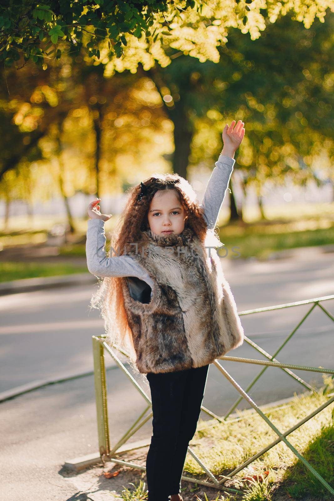 Stylish baby girl 4-5 year old wearing boots, fur coat standing in park. Looking at camera. Autumn fall season.